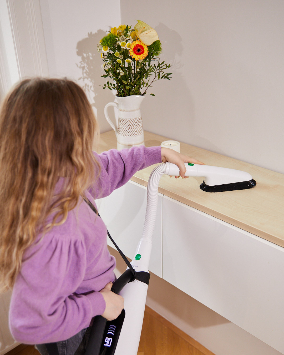 Frau saugt mit dem Kobold Handstaubsauger Staub von einem Sideboard – Szene aus der aime Kampagne „Mental (un)load“ für Vorwerk.